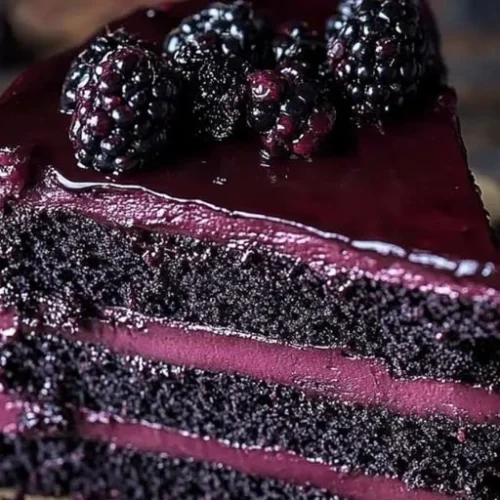 A slice of Blackberry Velvet Gothic Cake decorated with blackberries and dark icing.